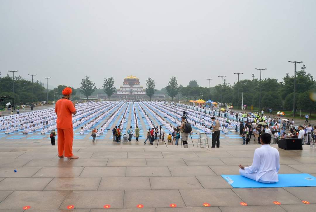 Stage-led meditation before rows of yoga practitioners
